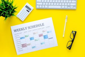 Weekly schedule of manager, office worker, pr specialist or marketing expert. Table with multicolored blocks on yellow office desk with computer, glasses, calculator top view